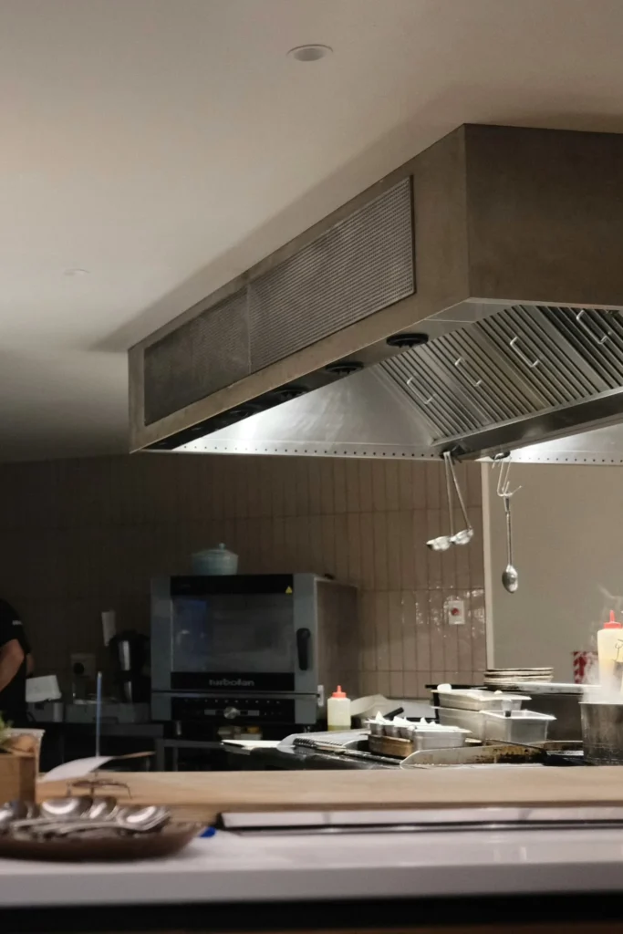 Stainless steel commercial kitchen canopy hood with baffle filters mounted above cooking equipment.